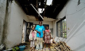 Ambuchu John is 58 years old and completely blind, seen here standing in his new home with his two eldest children, having been displaced by the fighting in Buea District, Cameroon.