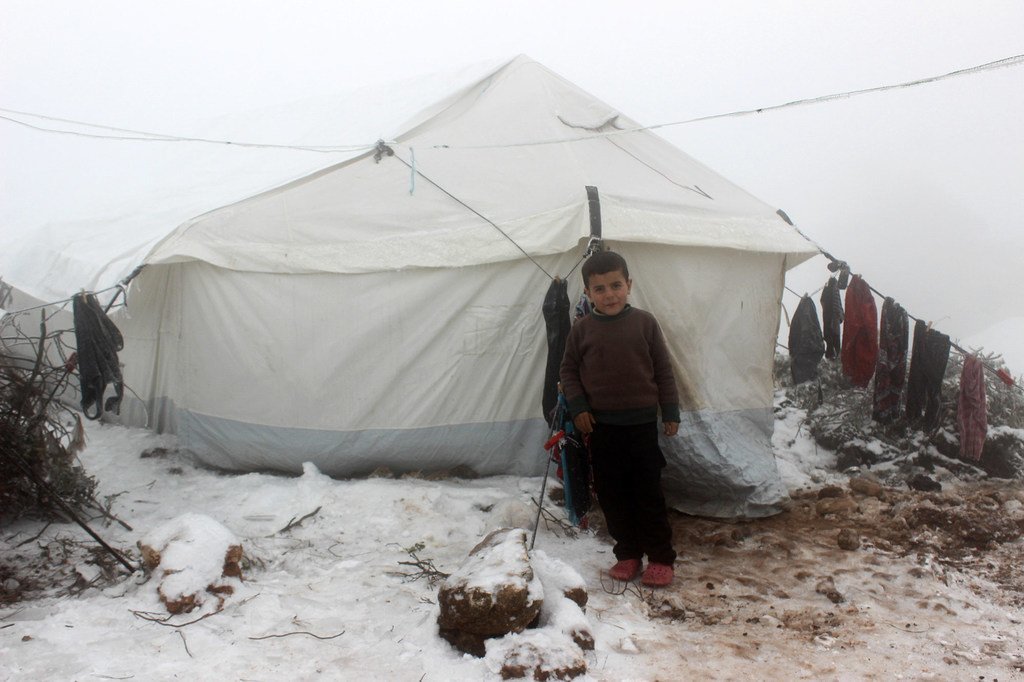 叙利亚西北部靠近土耳其边境的一处非正式定居点内，一个男孩站在一顶帐篷的入口处。