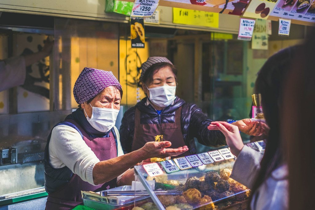 日本街头，一位店主戴着口罩售卖食品。
