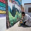 عضو في فريق "النقد مقابل العمل" الذي يدعمه برنامج الأمم المتحدة الإنمائي، يرسم لوحة جدارية في مدرسة للبنات غربي الموصل، في العراق.