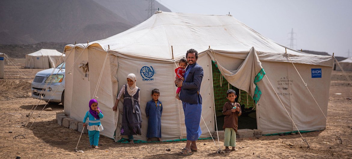 أب يقف مع أطفاله خارج خيمتهم في موقع للنازحين خارج مدينة مأرب باليمن.