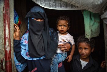 A displaced woman stands in the doorway of her shelter with her young children in Ibb city, Yemen.