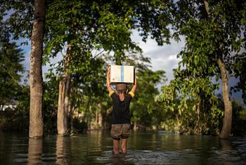 صبي يحمل صندوقًا من المساعدات الغذائية التي يقدمها برنامج الأغذية العالمي عبر مياه الفيضانات في بنغلاديش