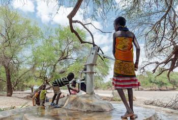 肯尼亚图尔卡纳县，一名年轻女孩在沙坝附近操作手摇水泵。