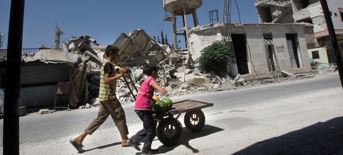 Young boys who work as market porters push a cart past ruins in Idlib, Syria.