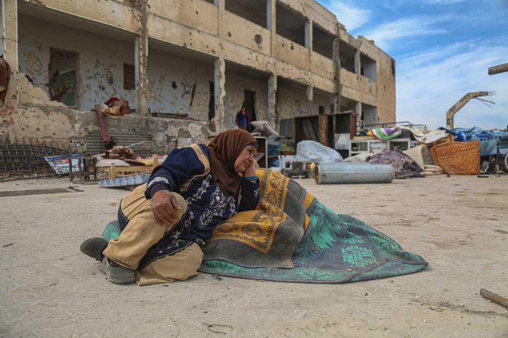 在叙利亚伊德利卜，一名流离失所的妇女坐在一所受损的学校外面的地上，这里是她现在的居所。