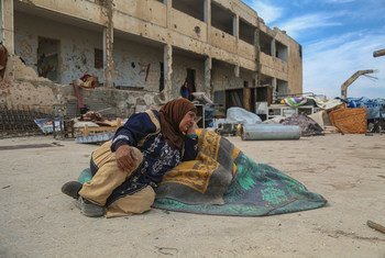 In Idlib, Syria, a displaced woman sits on the floor outside the damaged school that she now lives in.