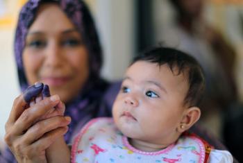 लीबिया चुनाव में, बेनग़ाज़ी में मतदान करने के बाद अपनी बेटी की इंक लगी उंगली दिखाती एक महिला.
