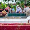 أسرة في إندونيسيا تزور قبر والدتهم التي كانت تعمل في أحد المطاعم الشهيرة حيث أصيبت بالفيروس هناك على الأرجح.