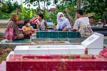 أسرة في إندونيسيا تزور قبر والدتهم التي كانت تعمل في أحد المطاعم الشهيرة حيث أصيبت بالفيروس هناك على الأرجح.