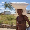 Mama mmoja mwenye tabasamu nchini Zimbabwe amebeba mfuko wa chakula cha msaada kichwani mwake.