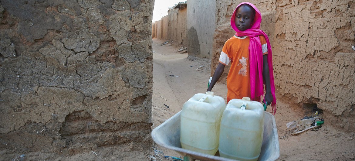 A nine-year-old girl pushes a wheelbarrow loaded with water-filled jerrycans in a IDP camp in Darfur, Sudan.