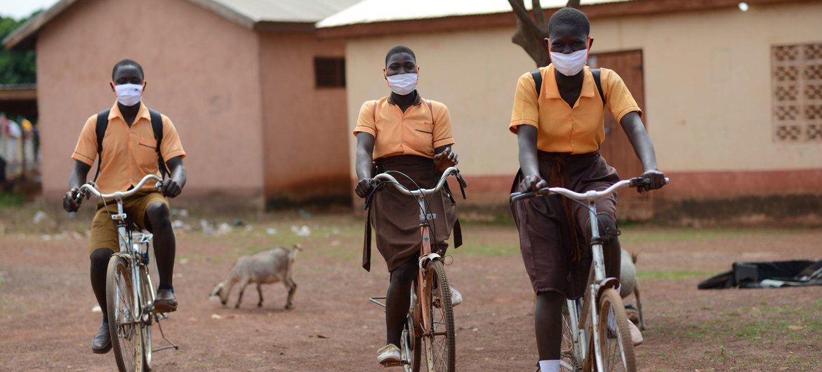 加纳的儿童戴着口罩骑自行车上学。