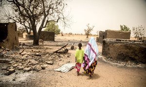 A woman and her daughter walk past the remains of destroyed homes during the March 2019 attack on Ogossagou village by armed Dogon men in which over 150 civilians were killed.