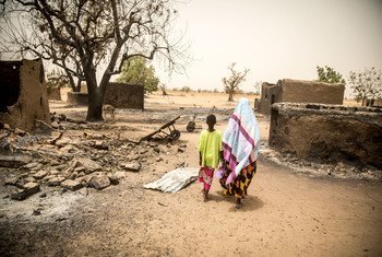 A woman and her daughter walk past the remains of destroyed homes during the March 2019 attack on Ogossagou village by armed Dogon men in which over 150 civilians were killed.