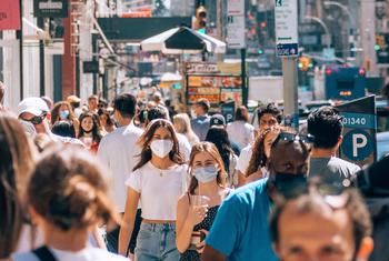 An uptick in COVID-19 cases in New York prompts people on a busy street to don protective masks.