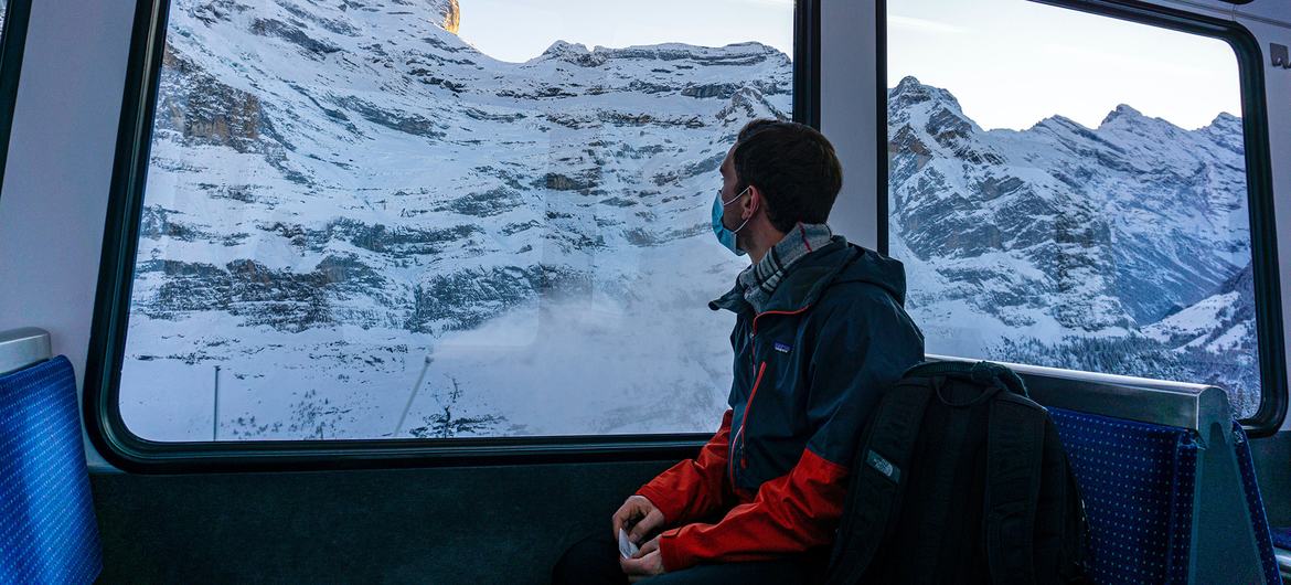 A young man travelling through the Swiss Alps by train during pandemic times.