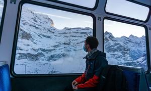 A young man travelling through the Swiss Alps by train during pandemic times.
