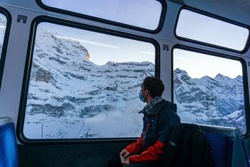 A young man travelling through the Swiss Alps by train during pandemic times.