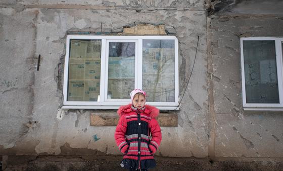 On 6 February 2022, a nine-year-old girl stands in front of the conflict-damaged exterior of her home in eastern Ukraine.