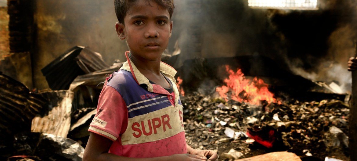 On 23 March, a ten-year-old child stands amidst debris at the Kutupalong refugee camp in southern Bangladesh. Behind him, the fire still burns, a day after the massive blaze tore through the camp.