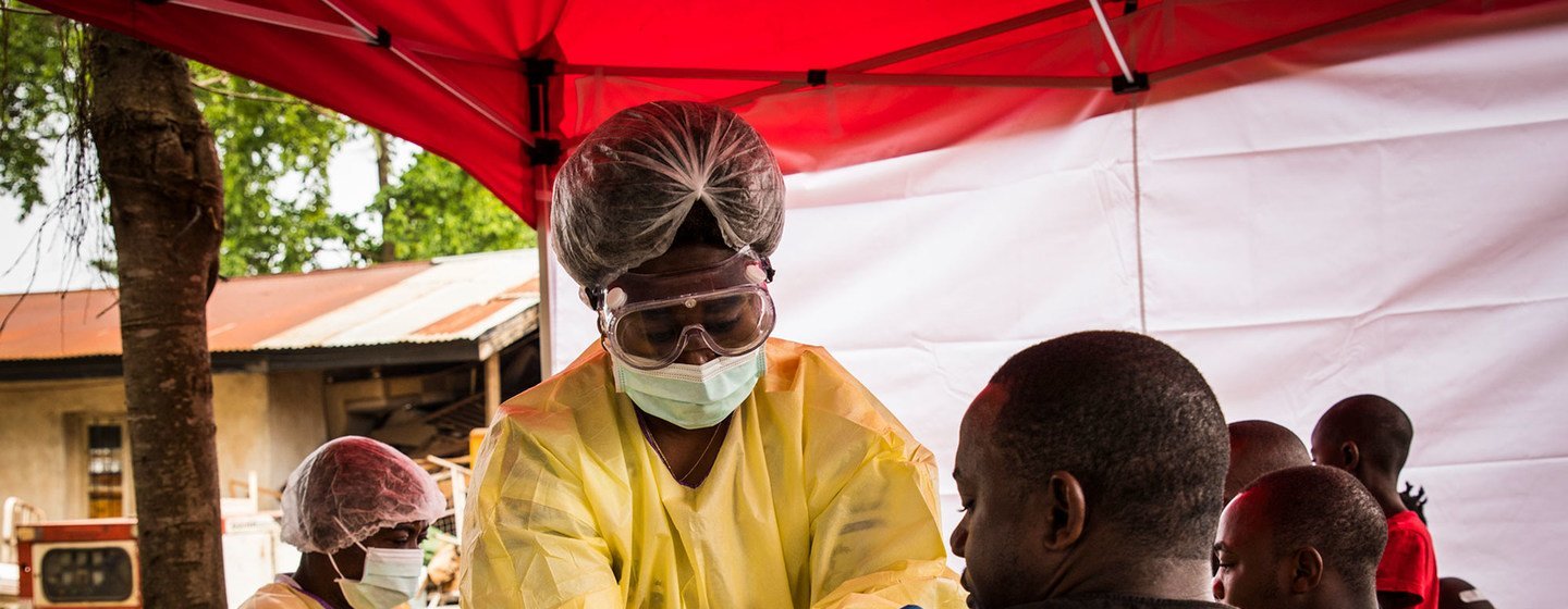 Um profissional de saúde, devidamente equipado com equipamento de proteção individual, administra a vacina contra o Ebola a um homem sob uma tenda vermelha em Beni, Kivu do Norte, República Democrática do Congo.