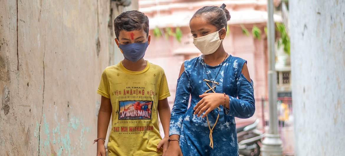 A young boy and girl in India protect themselves against COVID-19 by wearing face masks.