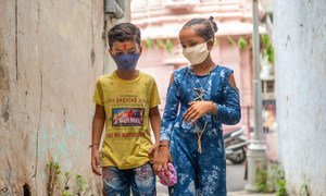 A young boy and girl in India protect themselves against COVID-19 by wearing face masks.