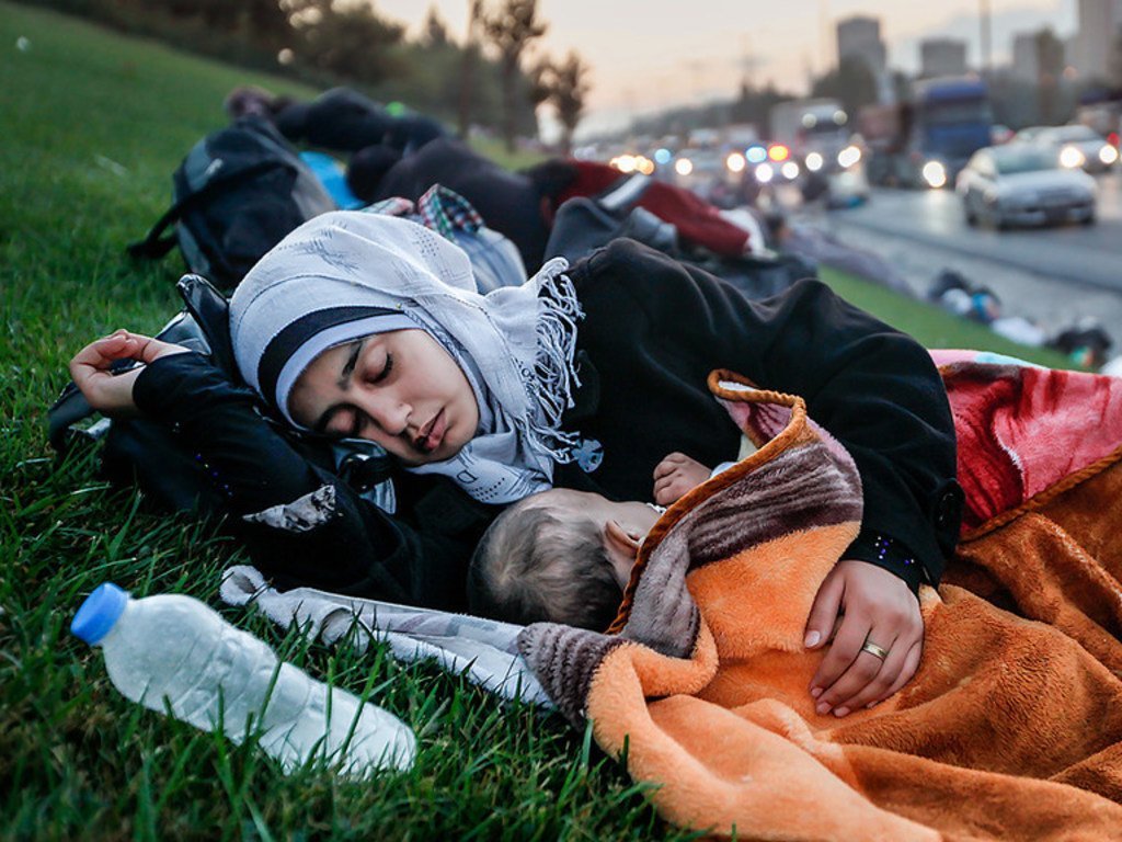 Una madre sin hogar duerme con su bebé en la hierba cercana a una autopista.