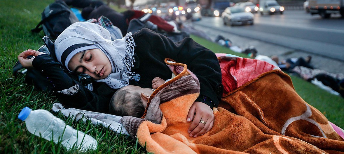 A homeless mother sleeping with her baby on a grass patch near highway.