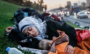 A homeless mother sleeping with her baby on a grass patch near highway.