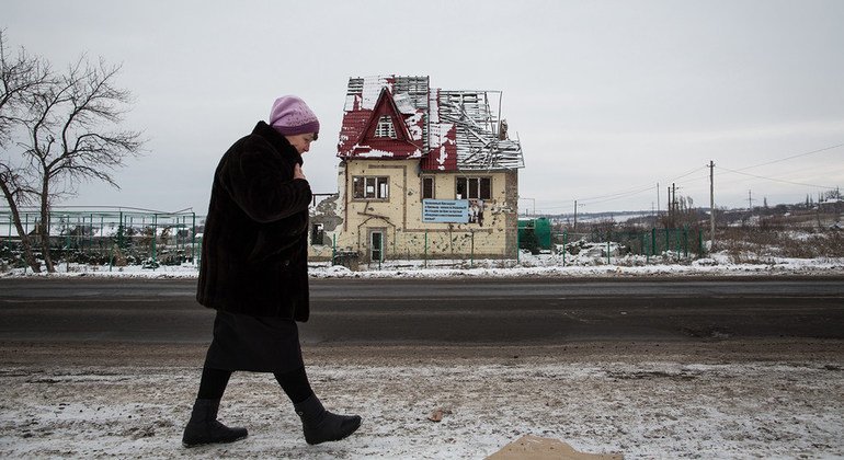 A woman in Ukraine passing by a war-ruined house.