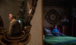Abel watches his granddaughter, Barbara, inside their home in the Tserovani displacement settlement in the Republic of Georgia. Barbara was born in displacement. 