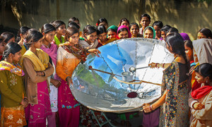 In India, a woman demonstrates how to use a solar dish for cooking.