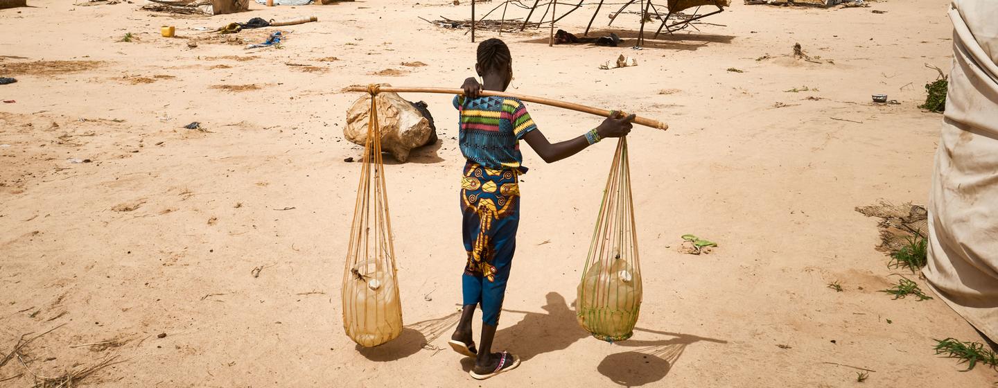 Une jeune femme porte de l'eau dans un camp de personnes déplacées dans la région de Tillaberi, au Niger.