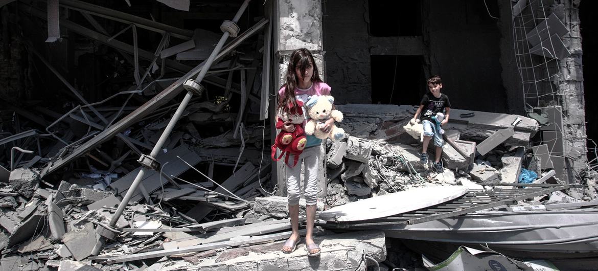 Una niña y un niño palestinos rescatan objetos del interior de su casa dañada en la ciudad de Gaza.