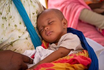 Un bebé duerme en los brazos de su madre en espera de recibir una vacuna.