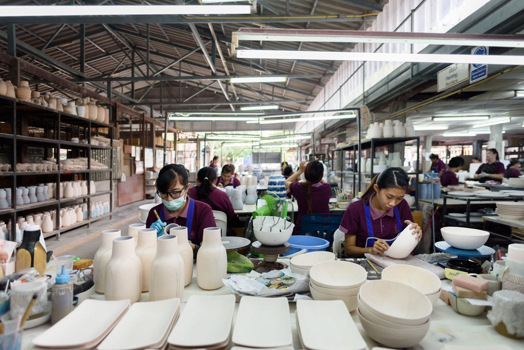 Thai women work at a ceramics factory in Chiang Mai, shaping and decorating pottery bowls and vases.