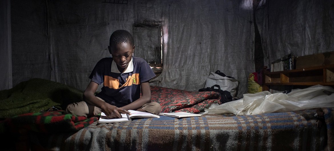 An 11-year-old child studies his Class 6 textbooks and revises the exercises at home in Nairobi, Kenya. He cannot participate in online learning as his family has no mobile phone.