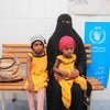 Una mujer con sus dos hijos en un centro de salud de Yemen. La niña del gorro rojo necesita tratamiento por desnutrición.