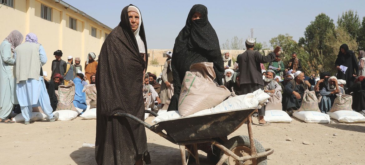 अफ़ग़ानिस्तान के हेरात में कुछ महिलाएँ, वितरण केन्द्र से खाद्य राहत सामग्री ला रही हैं. (2021)