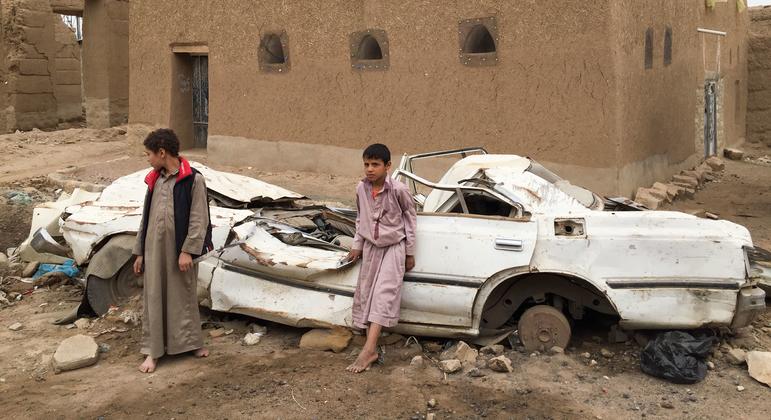 也门萨达，小男孩们站在一辆损坏的汽车前。