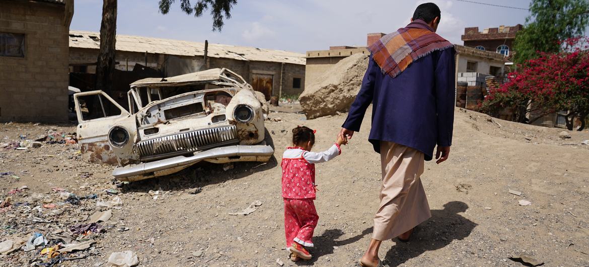 رجل يسير مع ابنته البالغة من العمر ثلاث سنوات في حي حارة المصنع الفقير في صنعاء، اليمن.