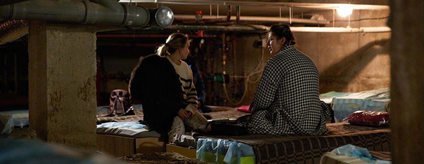 Deux femmes assisent sur des lits de fortune dans une cave en Ukraine.