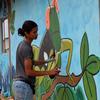 Una mujer está pintando un mural en una pared mientras dos niños la observan desde una ventana.