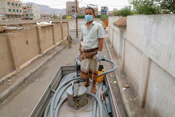 一名男子在一辆水车上工作，向也门萨那的社区供水。在新冠大流行期间，联合国儿童基金会为当地家庭提供清洁水。