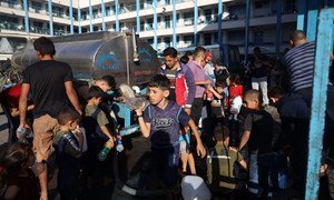 Children in Gaza gather at a water truck to fill bottles with clean drinking water. 
