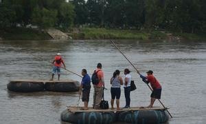 A group of people cross the Suchiate River on a raft, crossing the border between Guatemala and Mexico, in November 2021.