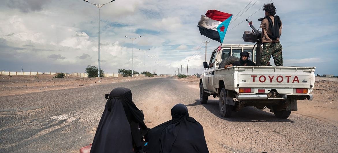 Veículos com soldados passa ao lado de mulheres pedindo ajuda em Lahj, Iêmen. 