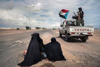 Veículos com soldados passa ao lado de mulheres pedindo ajuda em Lahj, Iêmen. 